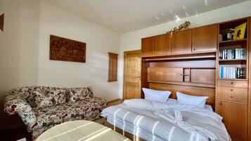 Un dormitorio con una cama, un armario de madera, un sofá floral y un cuadro en la pared.