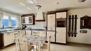 Una cocina con armarios blancos, una mesa de comedor con sillas, una ventana con cortinas y un bloque de cuchillos fijado a la pared.