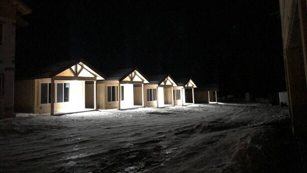 A row of wooden cabins with pitched roofs, each with a door and windows, set in a snowy landscape at night. - 2 Queen Beds, WIFI, Mini Fridge, Microwave, Full Bathroom (Island Park)