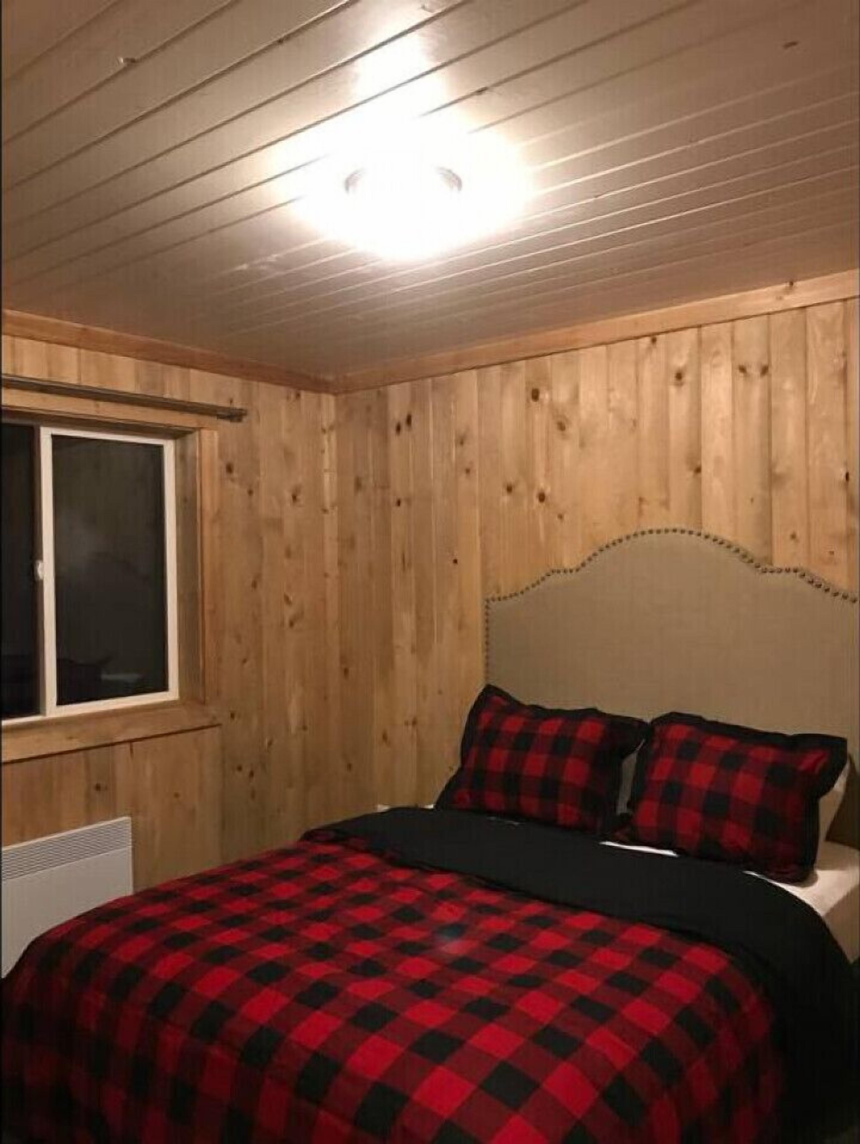 Un dormitorio con paneles de madera, una cama con colcha a cuadros rojo y negro, y una ventana con persianas.