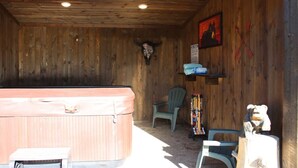 A wooden room with a hot tub, a chair, and a mounted animal skull. - Full Bathroom, 2 Queen Beds, WIFI, Shared Hot Tub (Island Park)