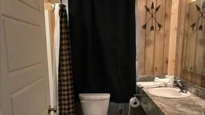 A compact bathroom with a toilet, sink, and shower curtain. - Shared Hot Tub, WIFI, 2 Queen Beds, Full Bathroom (Island Park)