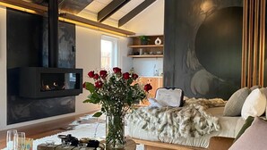 Ein modernes Wohnzimmer mit Kamin, rundem Holztisch, Sofa und einer Pendelleuchte.