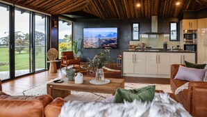 A spacious living area with a large TV, wooden ceiling, and a view of the outdoors. - Unique luxury + salvage + African theming = Heaven (Hepburn Springs)