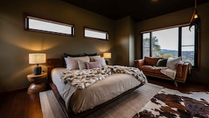 A bedroom with a large bed, two bedside tables, a leather sofa, and a view of the outdoors through large windows. - Unique luxury + salvage + African theming = Heaven (Hepburn Springs)