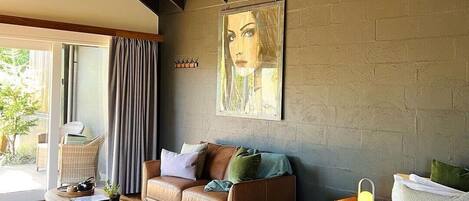 A modern bedroom with a large bed, a leather sofa, a wooden coffee table, and a large window with curtains.