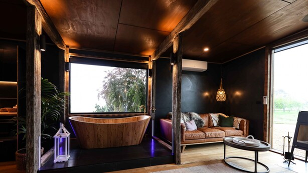 A modern interior with a wooden bathtub, leather sofa, and a large window.