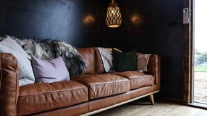 A brown leather sofa with a fur throw and pillows, a wooden floor, and a hanging light fixture.