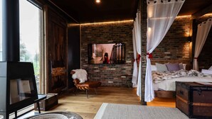 A cozy bedroom with a brick wall, a fireplace, a bed with white bedding, and a television.