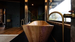 A modern bathroom with a wooden bathtub, a window with a view, and a rustic decor.