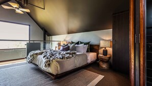 Un dormitorio moderno con una cama grande, un ventilador de techo, una mesita de noche con lámpara y vistas al exterior.