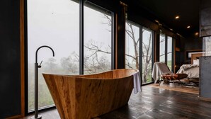 Un bagno moderno con una vasca freestanding, ampie finestre e vista sugli alberi.