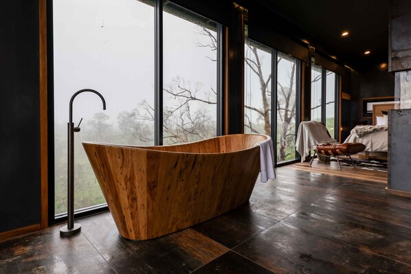 A modern bathroom with a freestanding bathtub, large windows, and a view of trees.