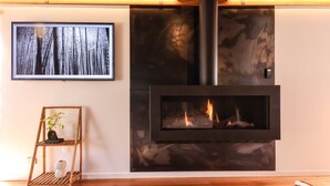 Ein modernes Wohnzimmer mit Kaminofen, einem gerahmten Bild von Bäumen und einem Holzregal mit Pflanze.
