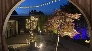 A circular wooden frame with a view of a house, string lights, and a tree.