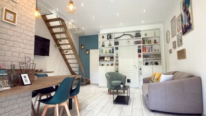 A modern living room with a wooden staircase, a dining area with chairs, a sofa, and a bookshelf. - Cosy duplex - between lakes and mountains - NO PARTIES ALLOWED (Fillinges)