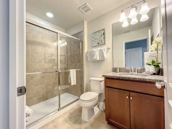 A modern bathroom with a glass-enclosed shower, a white toilet, and a vanity with a mirror.