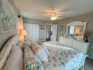 Une chambre à coucher avec un lit, une commode, un ventilateur de plafond et une porte.