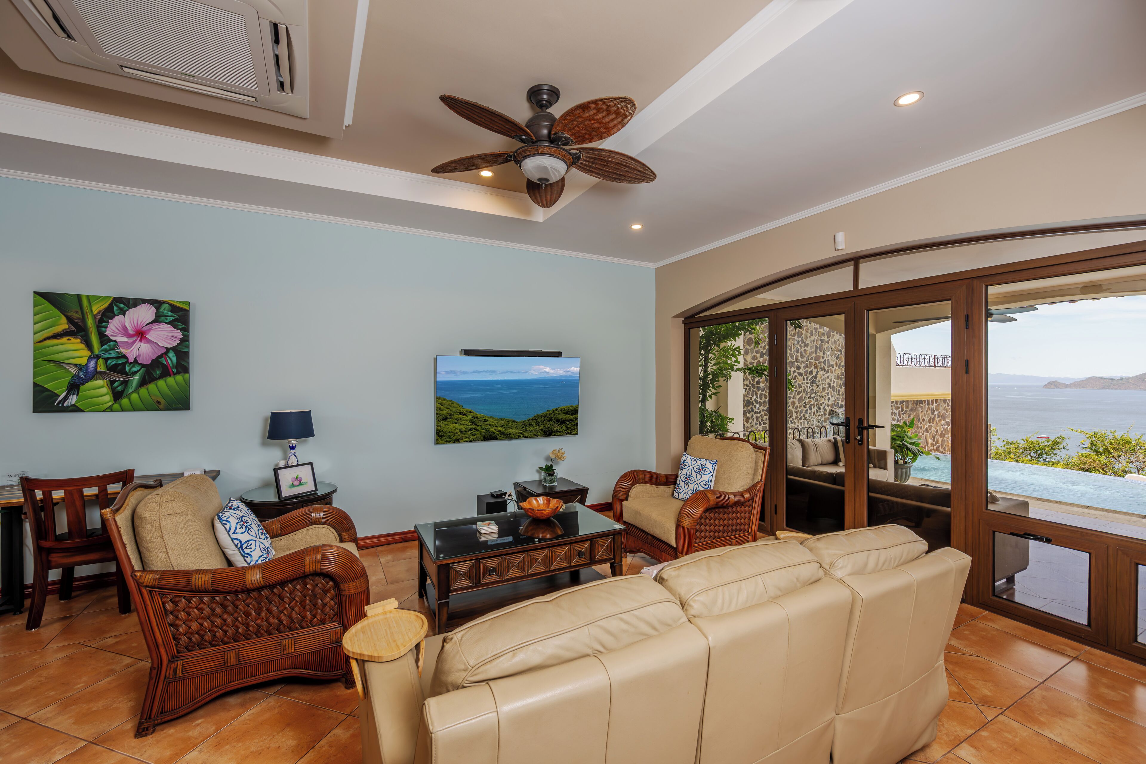 A spacious living room with a large leather sofa, wicker chairs, a coffee table, and a ceiling fan.