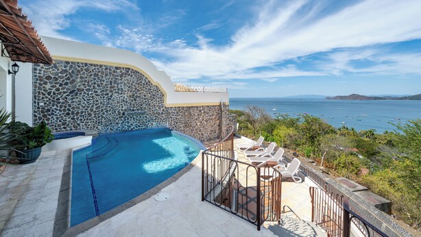 A pool area with a stone wall, lounge chairs, and a view of the sea. - Mariners Point C1 – 3-Bedroom Villa on Bluff Above Playa Hermosa with Private Pool (Playa Hermosa)