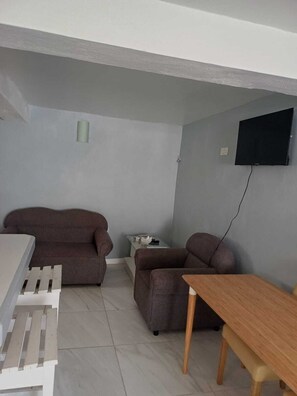 A small living room with a sofa, a table, and a TV mounted on the wall. - Village Comfort  (Belmont)