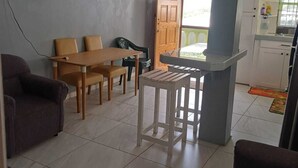 A dining area with a wooden table and chairs, a small white stool, and a grey pillar. - Village Comfort  (Belmont)