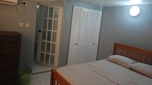 A bedroom with a bed, a wooden dresser, a wardrobe, and a door leading to another room. - Village Comfort  (Belmont)