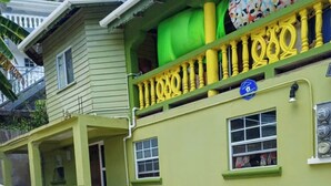 A two-story building with a green facade, a balcony with yellow balustrades, and a visible blue sign. - Village Comfort  (Belmont)