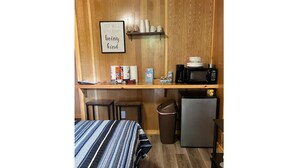 A small kitchenette with a microwave, coffee maker, and a trash bin. There is a bed with a striped bedspread and a framed quote on the wall. - Studio Cabin – Pet-Friendly Retreat Near Lake Greeson & Kirby Landing Marina (Kirby)