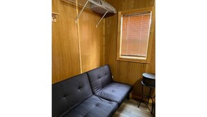 A room with a black sofa, a small round table, and a window with blinds. - Studio Cabin – Pet-Friendly Retreat Near Lake Greeson & Kirby Landing Marina (Kirby)