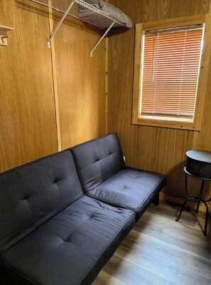 Une pièce avec un canapé noir, une petite table ronde et une fenêtre avec des stores.