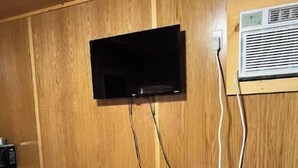 A room with a mounted television, a small black shelf with items, and a wall-mounted air conditioning unit. - Studio Cabin – Pet-Friendly Retreat Near Lake Greeson & Kirby Landing Marina (Kirby)