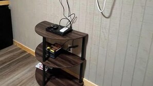 Una habitación con una televisión de pantalla plana montada en la pared, un mueble de madera para entretenimiento con dispositivos electrónicos y un equipo de aire acondicionado.