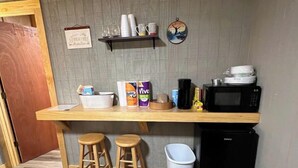 Cocina compacta con encimera de madera, dos taburetes, microondas y un cubo de basura.