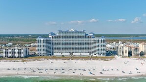 A large hotel with multiple floors, a beach in the foreground, and a clear sky.