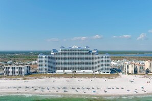 A large hotel with multiple floors, a beach in the foreground, and a clear sky.