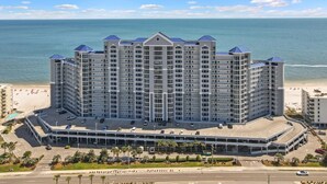 A high-rise hotel with multiple balconies, a parking garage, and a beach view.