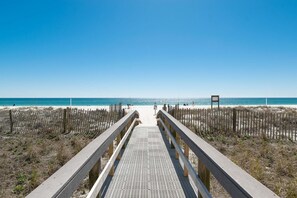 Une promenade en bois menant à une plage, avec un ciel dégagé.