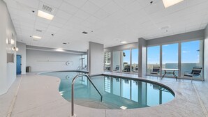 A large indoor swimming pool with a curved design, surrounded by a tiled floor and a glass wall.