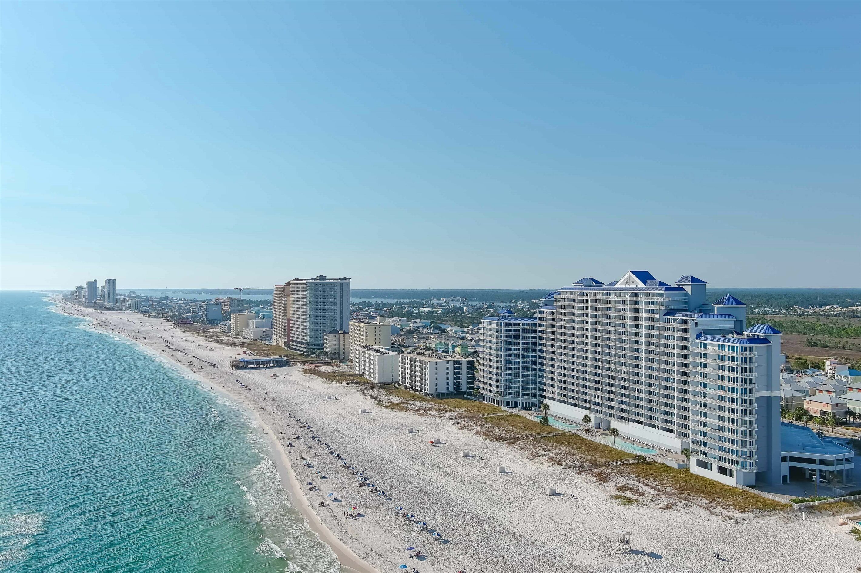 A coastal hotel with multiple floors, a beach view, and a pool area.