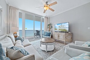 A living room with a sofa, armchairs, a coffee table, a ceiling fan, a television, and a view of the outdoors.