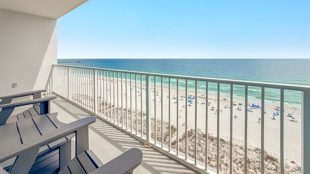A balcony with a view of a beach, a table, and a bench.