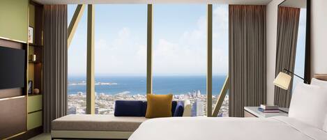 A hotel room with a large bed, a sofa, a TV, and a view of the city and ocean.