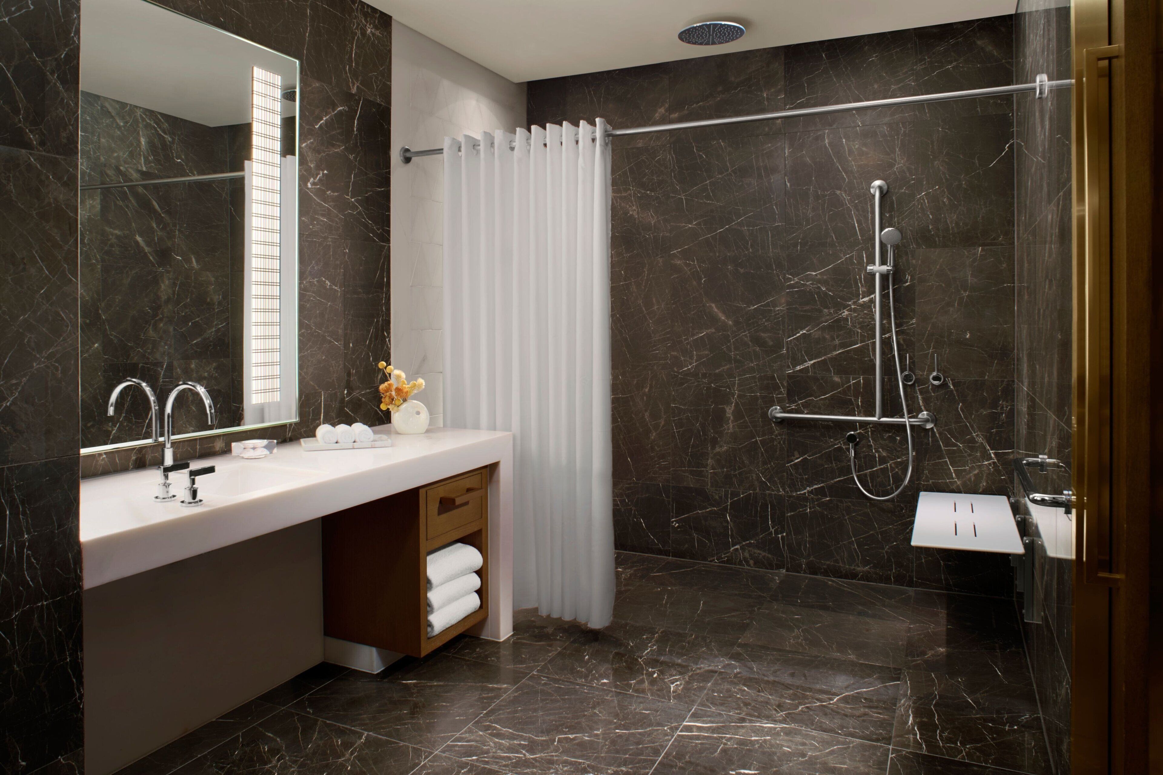 Un baño moderno con piso de mármol, un lavamanos blanco con espejo, una ducha con puerta de vidrio y un perchero para toallas.