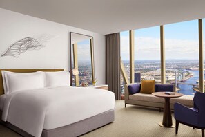 A hotel room with a large bed, a sofa, a small table, and a view of a cityscape through large windows. - The Ritz-Carlton, Melbourne (Melbourne)