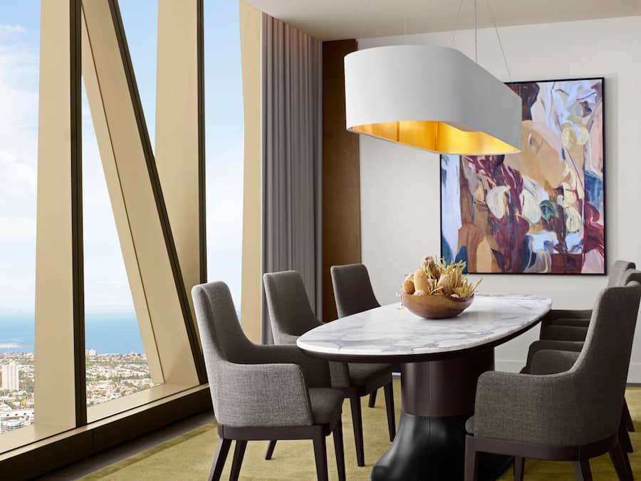 A modern dining area with a round table, six grey upholstered chairs, a marble top, and a large abstract painting on the wall.