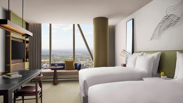 A hotel room with a large bed, a desk, a chair, a sofa, and a view of the city.