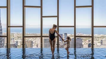 A woman and a child in a large indoor pool with a city view through large windows.