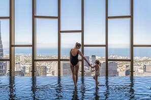 A woman and a child in a large indoor pool with a city view through large windows.
