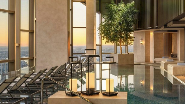Een modern binnenzwembad met glazen balustrades, een centrale zithoek en een stadszicht door grote ramen.